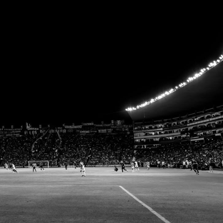 A well-lit, packed soccer stadium at night with players running about on the field.